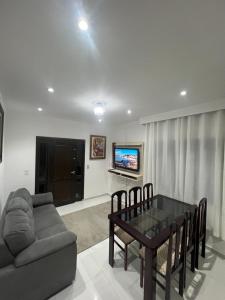 ein Wohnzimmer mit einem Tisch, einem Sofa und einem TV in der Unterkunft RECANTO RESIDENCIAL MARISCAL APT03 in Bombinhas