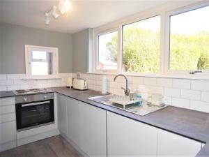 a kitchen with white cabinets and a sink and windows at Little Trevarrack in Carbis Bay