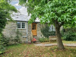 una casa in pietra con una panchina e un albero di Gardeners Cottage a Mudford