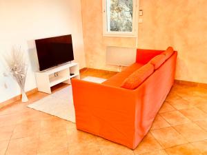 - un canapé orange dans le salon avec une télévision dans l'établissement Provencal villa with stunning view & summer pool, à Rochefort-du-Gard