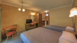 a bedroom with two beds and a desk with a television at Barrass's John Bright Motor Inn in Bright