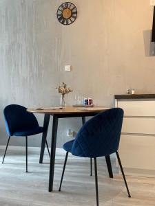 een eettafel met 2 stoelen en een klok aan de muur bij Apartamet Poezji A04 Blue in Gliwice