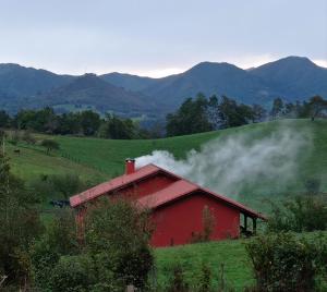 Torío的住宿－La Casona de Torió，一片田野里的一个红谷仓,烟从里面冒出来
