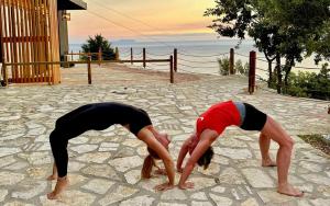 two women doing a yoga pose on a stone ground at Rahoni Park & Suites in Dhërmi