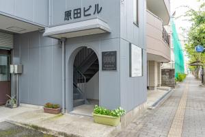 佐賀インターナショナルゲストハウスHAGAKURE 2号店 في ساغا: مدخل لمبنى به مدخلات ورد على رصيف