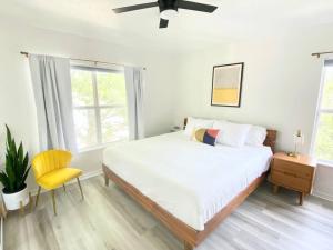 a white bedroom with a bed and a yellow chair at Sanctuary Gainesville Bright 2 BR King Condo in Gainesville