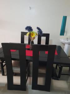 una mesa de comedor negra con 2 sillas y un jarrón con flores en Jacky's Milimani suites, en Nakuru