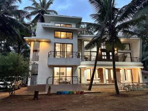 une grande maison blanche avec des palmiers devant elle dans l'établissement SeaLaVie Sea View Farmhouse, à Nandgaon