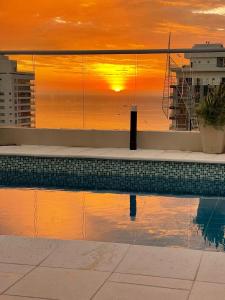 a swimming pool with a sunset in the background at Apartasuite moderno y elegante en Playa Salguero in Gaira