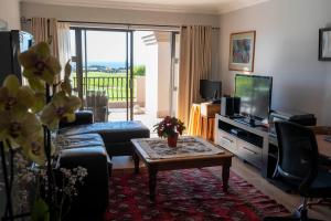 uma sala de estar com um sofá, uma televisão e uma mesa em Fairways Apartment Mossel Bay Golf Estate em Mossel Bay