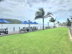 a park with picnic tables and blue umbrellas next to the water at Modern 2Bedroom Self Catering unit HBos. in Mossel Bay