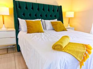 ein weißes Bett mit gelben Kissen und einem grünen Kopfteil in der Unterkunft Genesis Guesthouze in Bela-Bela