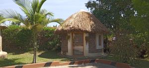 une petite cabane avec un toit de paille et un palmier dans l'établissement Plastic Bottles House, à Entebbe