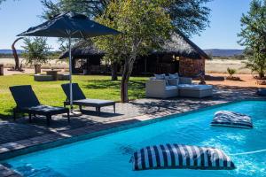 a swimming pool with two chairs and an umbrella at Arnhem Cave Lodge in Omitara