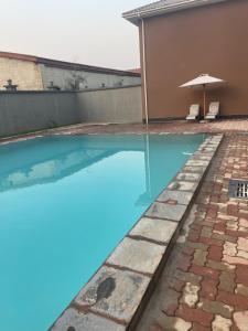 een zwembad naast een huis met een parasol bij Njikale Number 3 in Lusaka