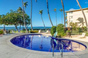 a swimming pool with palm trees and the ocean in the background at Kanai A Nalu 202 in Wailuku