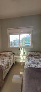 Un dormitorio con dos camas y una ventana. en Apartamento uma quadra do mar, melhor localização, en Capão da Canoa