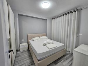 een witte slaapkamer met een bed en een raam bij Tirana Apartment Comfort Home in Tirana