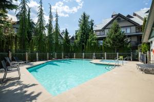 a large swimming pool with chairs and a fence at Steps From The Village with Pool and Hot Tub by Harmony Whistler in Whistler
