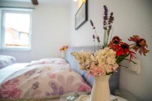 eine weiße Vase mit Blumen auf einem Tisch neben einem Bett in der Unterkunft Ferienhaus Simone in Neuwerk