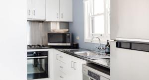 a white kitchen with a sink and a microwave at Pattys Cottage - Pet friendly home in Merewether in Merewether