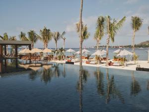 una piscina con palmeras y sombrillas en la playa en BASK Gili Meno, en Gili Meno