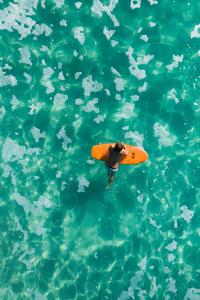 Ein Mann, der mit einem Surfbrett im Wasser schwimmt in der Unterkunft Pebbly Beach Escape in East Lynne