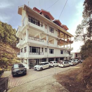 西姆拉的住宿－The MoonLight Stay - Shimla，一座白色的建筑,前面有汽车停放