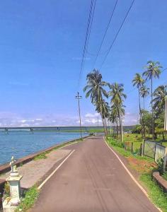 an empty road next to the ocean with palm trees at Baga Beach Prime in Baga