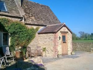 Battens Farm Cottages B&B في Yatton Keynell: مبنى حجري مع كرسيين وباب