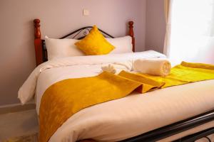 Una cama con sábanas amarillas y toallas. en MORNINGSTAR 2BR APARTMENTS IN NAKURU en Nakuru