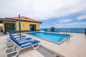 a swimming pool with blue lounge chairs and the ocean at Shell House by GALMI in Arco da Calheta