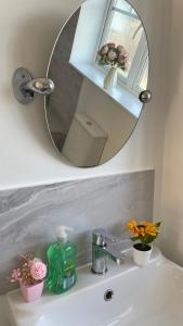a bathroom sink with a mirror and flowers on it at Stylish 4beds home, perfect for Company contractors and family stays - NEC, Airport, HS2, Resort World in Marston Green