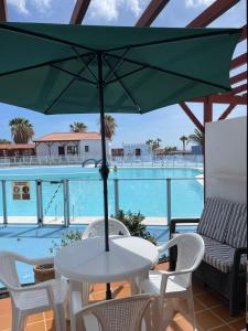 Una mesa con una sombrilla verde en un balcón con piscina. en Sun Beach 10, en Caleta de Fuste