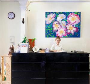 une femme assise à un bureau dans une pièce avec une peinture dans l'établissement Jade Hotel, à Hue