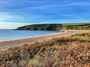 a sandy beach next to a large body of water at Beach Woods Coastal Path chalet in Pembrokeshire