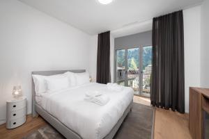 a bedroom with a white bed and a large window at Swiss Hotel Apartments - Engelberg in Engelberg