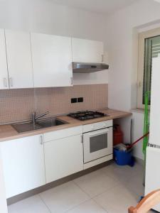 una cucina con armadi bianchi, lavandino e piano cottura di Casa vacanze sul mare a SantʼAlessio Siculo