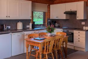 a kitchen with white cabinets and a wooden table and chairs at Armadale Castle Cabins in Ardvasar