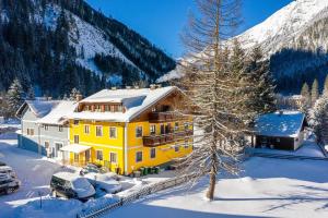 a yellow house in the snow with a tree at Appartementhaus zur Post in Bad Gastein