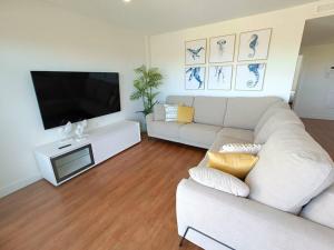 ein Wohnzimmer mit einem weißen Sofa und einem Flachbild-TV in der Unterkunft Nuevo Ático Toyo. Vistas al mar, terraza, solarium, piscina, A/A, WiFi y Garaje in El Toyo