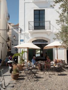 two people sitting at tables with umbrellas in front of a building at Can Set in Cadaqués