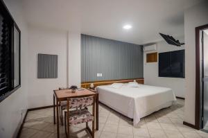 a bedroom with a white bed and a table and a television at Alpes Hotel in Venda Nova do Imigrante