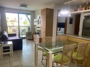 cocina y sala de estar con mesa de cristal y sillas en Marulhos Resort Beach - 2 quartos & 1 quarto, en Porto de Galinhas