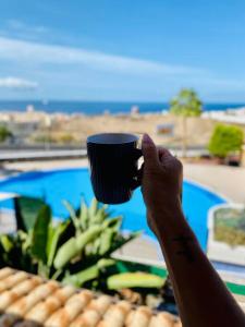 una persona che tiene una tazza di caffè di fronte alla piscina di Golden Suite Ocean View & Pool a Los Cristianos