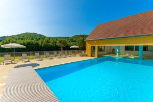 une grande piscine bleue avec des chaises et une maison dans l'établissement Lagrange Vacances Les Bastides de Lascaux, à Montignac