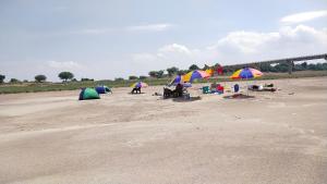 un grupo de personas sentadas bajo sombrillas en una playa en Jhoomke camping and water sports adventure en Auraiya
