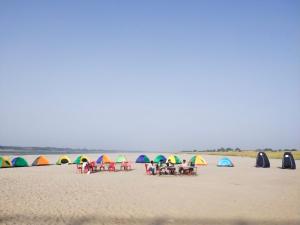 a group of people sitting on a beach with tents at Jhoomke camping and water sports adventure in Auraiya