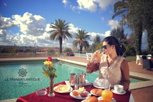 Una donna seduta a un tavolo con del cibo vicino alla piscina di Hotel Transatlantique a Meknès