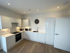a kitchen with white cabinets and a clock on the wall at Beachfront Bliss Apartment - Near Hythe - On Beach Seafront - Private Parking in Dymchurch